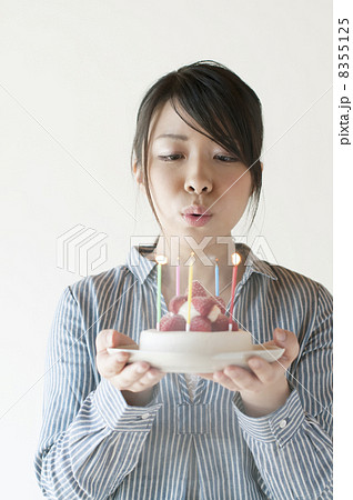 ケーキのろうそくの火を吹き消す女性の写真素材