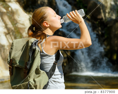Young woman drinks water by waterfall 8377900