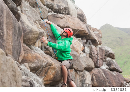 Fit man scaling a large rock face Fit man scaling a large rock face 8383021