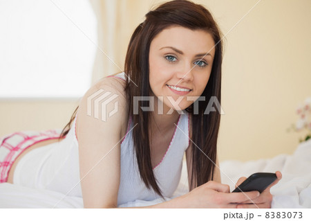 Smiling girl looking at camera using a mobile phone lying on a b Smiling girl looking at camera using a mobile phone lying on a b 8383073