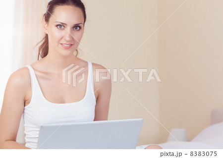 Happy brunette sitting on bed using her laptop 8383075