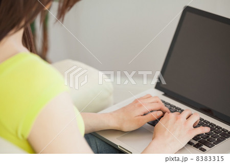 Girl typing on laptop sitting on a sofa Girl typing on laptop sitting on a sofa 8383315