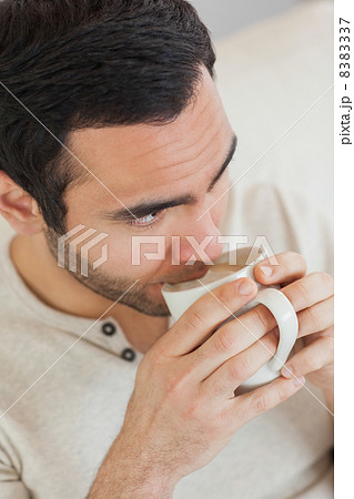 Thoughtful handsome man drinking coffee while relaxing on sofa 8383337