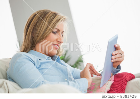 Smiling woman lying on a sofa using a tablet pc Smiling woman lying on a sofa using a tablet pc 8383429
