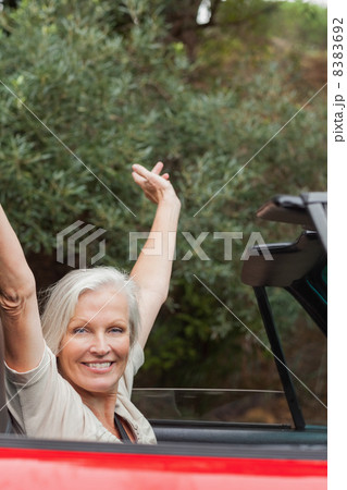 Cheerful mature woman enjoying her red convertible 8383692