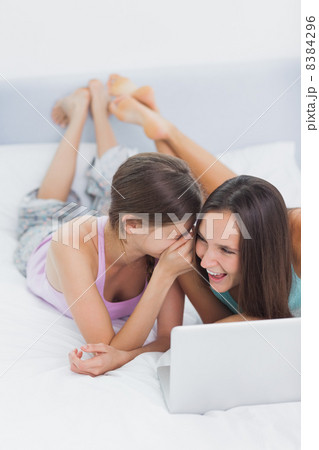 Friends lying in bed in pajamas with laptop Friends lying in bed in pajamas with laptop 8384296