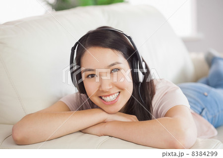 Smiling asian girl lying on the sofa and listening to music Smiling asian girl lying on the sofa and listening to music 8384299