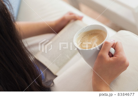 Woman lying on the sofa reading a book holding her coffee 8384677