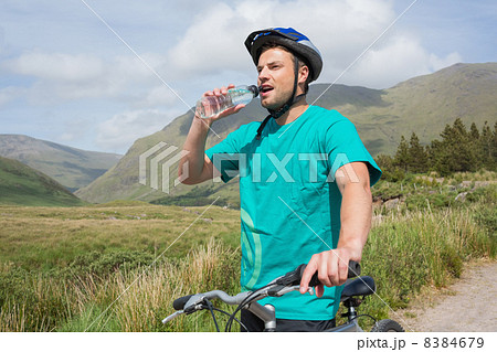 Fit man leaning on his mountain bike drinking water Fit man leaning on his mountain bike drinking water 8384679