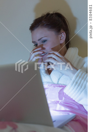 Pretty teen wearing dressing gown watching a scary movie on lapt Pretty teen wearing dressing gown watching a scary movie on lapt 8384681