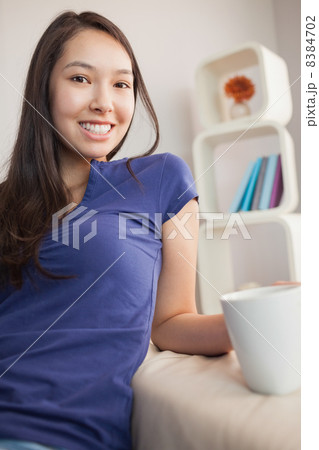 Happy young asian woman sitting on the couch holding mug Happy young asian woman sitting on the couch holding mug 8384702