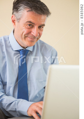 Pleased man using a laptop sitting on a bed Pleased man using a laptop sitting on a bed 8385062