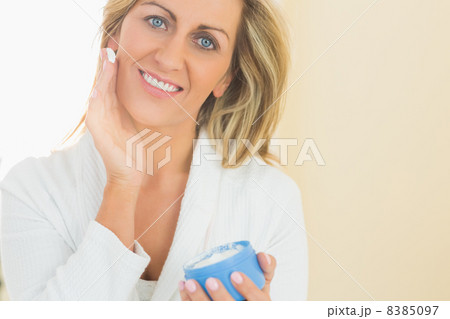 Pleased woman holding a jar of face cream in a hand and applying Pleased woman holding a jar of face cream in a hand and applying 8385097