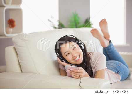 Smiling asian girl lying on the sofa and listening to music with Smiling asian girl lying on the sofa and listening to music with 8385388