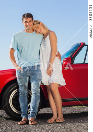 Happy cute couple posing against their red cabriolet Happy cute couple posing against their red cabriolet 8385551