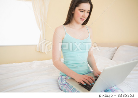 Smiling girl using a laptop sitting on her bed 8385552