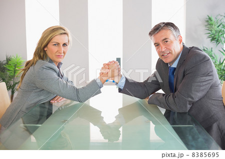 Two serious businesspeople having an arm wrestling sitting aroun 8385695