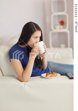 Woman sitting on the sofa drinking coffee with a pastry Woman sitting on the sofa drinking coffee with a pastry 8385818
