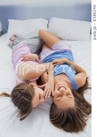 Girl whispering into her laughing friends ear Girl whispering into her laughing friends ear 8386240