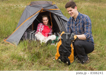 Happy man packing backpack while girlfriend sits in tent 8386241