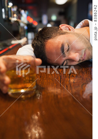 Unconscious businessman holding whiskey lying on a counter 8386242