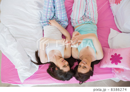 Pretty friends in pajamas looking at smartphone on bed 8386274