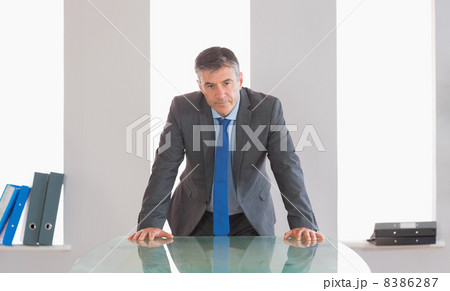 Frowning businessman standing in front of a desk 8386287
