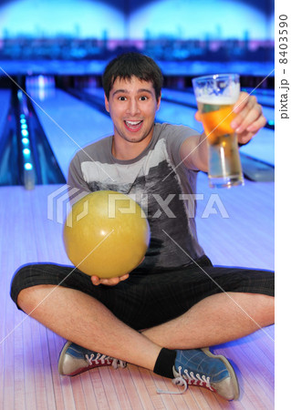Happy young man sits on floor and holds ball and glass of beer i Happy young man sits on floor and holds ball and glass of beer i 8403590