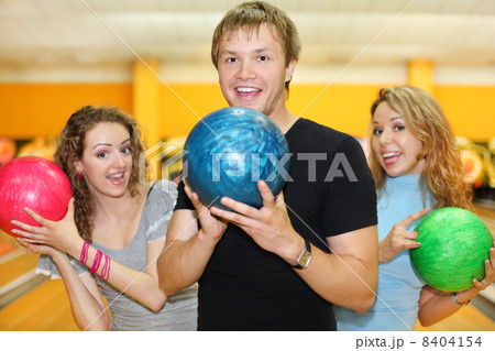Young man and two happy beautiful girls hold balls in bowling cl Young man and two happy beautiful girls hold balls in bowling cl 8404154