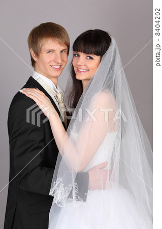 Happy young groom and bride embrace in studio on gray background Happy young groom and bride embrace in studio on gray background 8404202