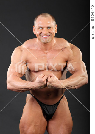 Undressed bronzed smiling bodybuilder demonstrates his arm muscl 8404218