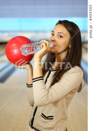 Young brunette woman holds red ball and drinks pure water from b 8404305