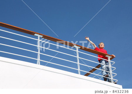 Boy stands at railing on deck of ship, shouts and waves his hand 8432236