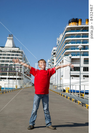 little boy spread hands against background two ships in Tallinn port, front view 8432467
