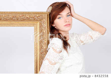 Beautiful melancholic woman in white dress stands near big gilt Beautiful melancholic woman in white dress stands near big gilt 8432558