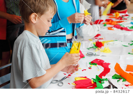 Boy makes artificial flower of tissue paper by stapler near tabl Boy makes artificial flower of tissue paper by stapler near tabl 8432617