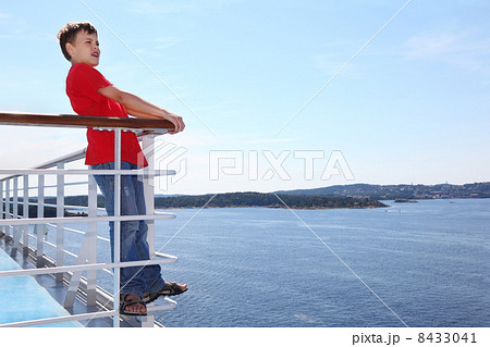 Boy stands at railing on deck of ship, looks into distance and s Boy stands at railing on deck of ship, looks into distance and s 8433041