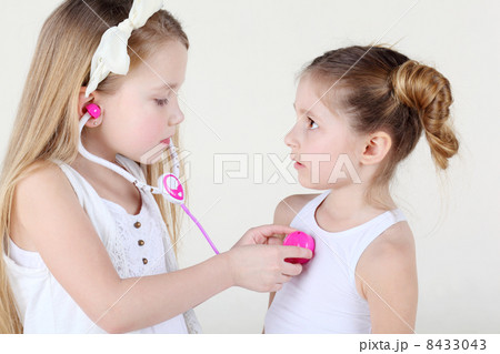Little girl in white listens heartbeat of another frightened gir 8433043