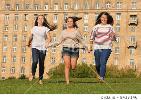 Three smiling girls run at green grass at background of multi-st Three smiling girls run at green grass at background of multi-st 8433146