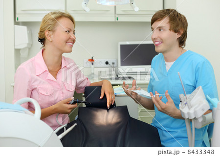Two smiling dentists sits in cabinet of dental clinic and look a Two smiling dentists sits in cabinet of dental clinic and look a 8433348
