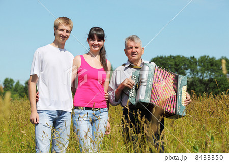 couple stand near grandfather with accordion in field near wood 8433350