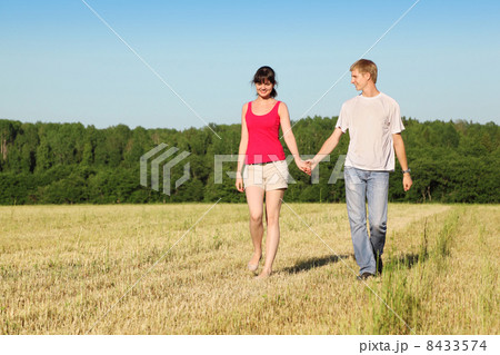 Husband, wife holding hands walk in field near wood Husband, wife holding hands walk in field near wood 8433574