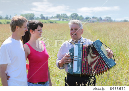 Grandfather in shirt play on accordion, sink for young couple near village 8433652