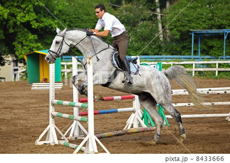Jockey in glasses jump on horse over barrier on hippodrome 8433666