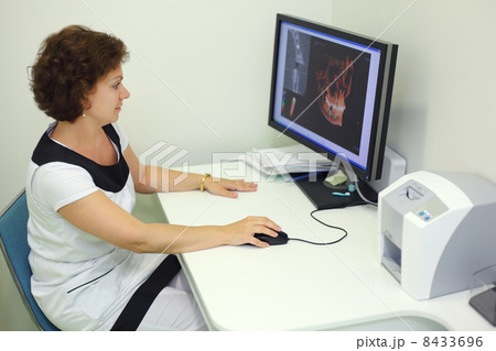 Dentist carefully looks skull X-rays at computer monitor in dent Dentist carefully looks skull X-rays at computer monitor in dent 8433696