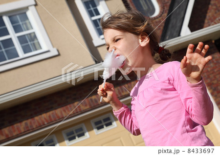 Happy little girl eats cotton candy and looks into distance near Happy little girl eats cotton candy and looks into distance near 8433697