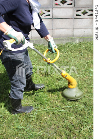 家庭用電動草刈機で庭の草刈りをする中年女性 家庭用電動草刈機で庭の草刈りをする中年女性 8441341