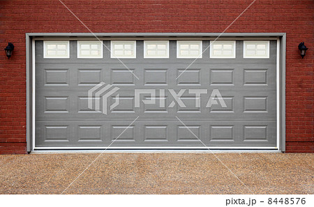 Big garage with gray doors, brick wall and asphalt driveway 8448576