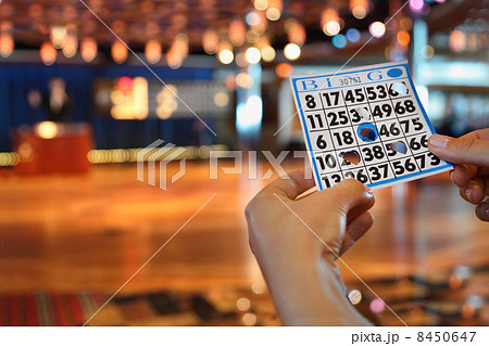 Hands hold bingo card with holes at background of big board Bing 8450647