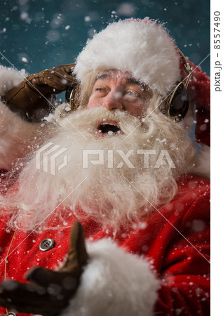 Santa Claus is listening to music in headphones outdoors at Nort Santa Claus is listening to music in headphones outdoors at Nort 8557490
